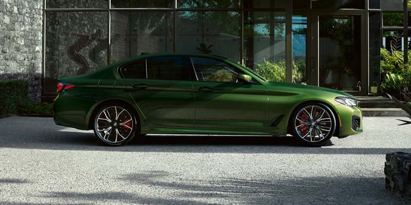 Dark green luxury sedan parked on a light-colored driveway in front of a modern building