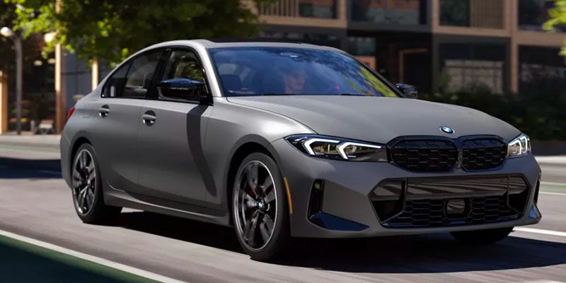 A matte gray BMW sedan driving on a city street in daylight