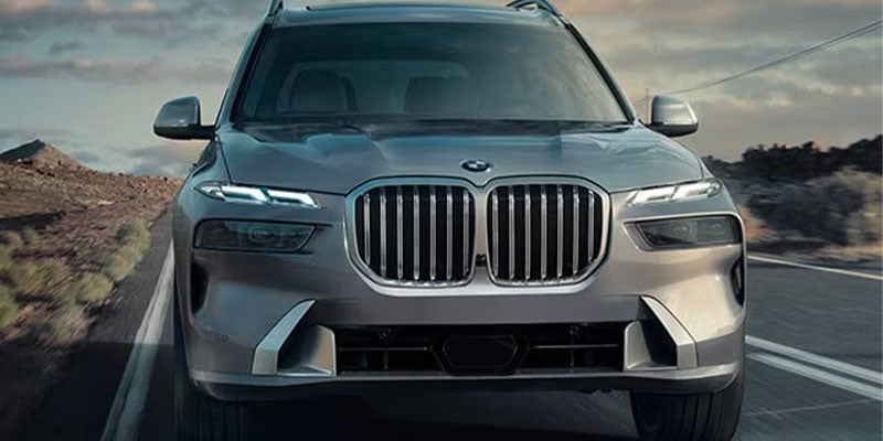 Front view of a silver BMW SUV driving on a paved road, featuring the brand’s signature kidney grille and LED headlights