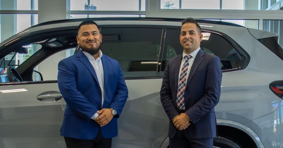 Two people are standing side-by-side in front of the SUV, facing the camera